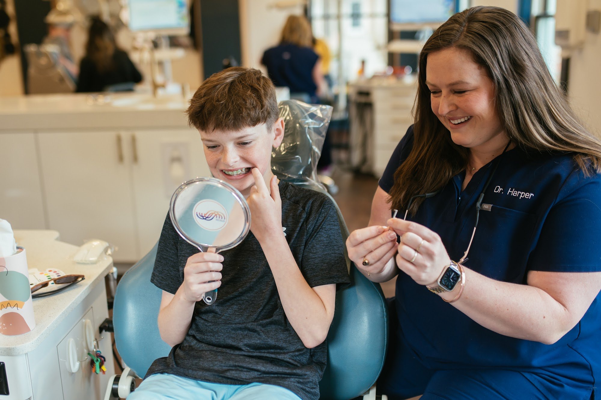 Anne Miller Harper, DMD, MSD, smiling with a boy as he checks his new braces in a hand mirror