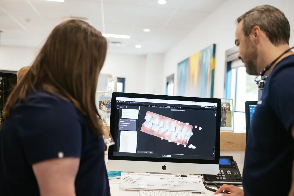 Orthodontist and team member reviewing a 3D digital model of a patient's teeth on a computer screen